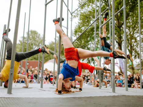 Dancers in bright clothing doing handstands among metal scaffolding
