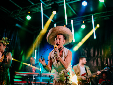 A singer in a large straw hat performs with a band.
