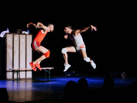 Two performers dressed in white and red boxing wear pose in mid air.