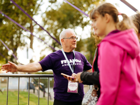 A smiling volunteer in a purple t-shirt directs a crowd.